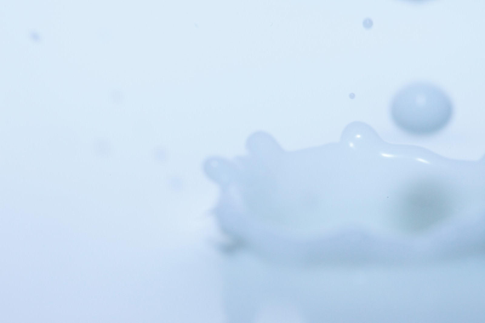 淡い青の水面に落ちた雫が王冠状の飛沫を上げ、小さな水玉が散っている様子