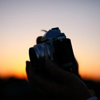 夕焼け空をバックにシルエットで写る手に持ったミラーレスカメラの写真