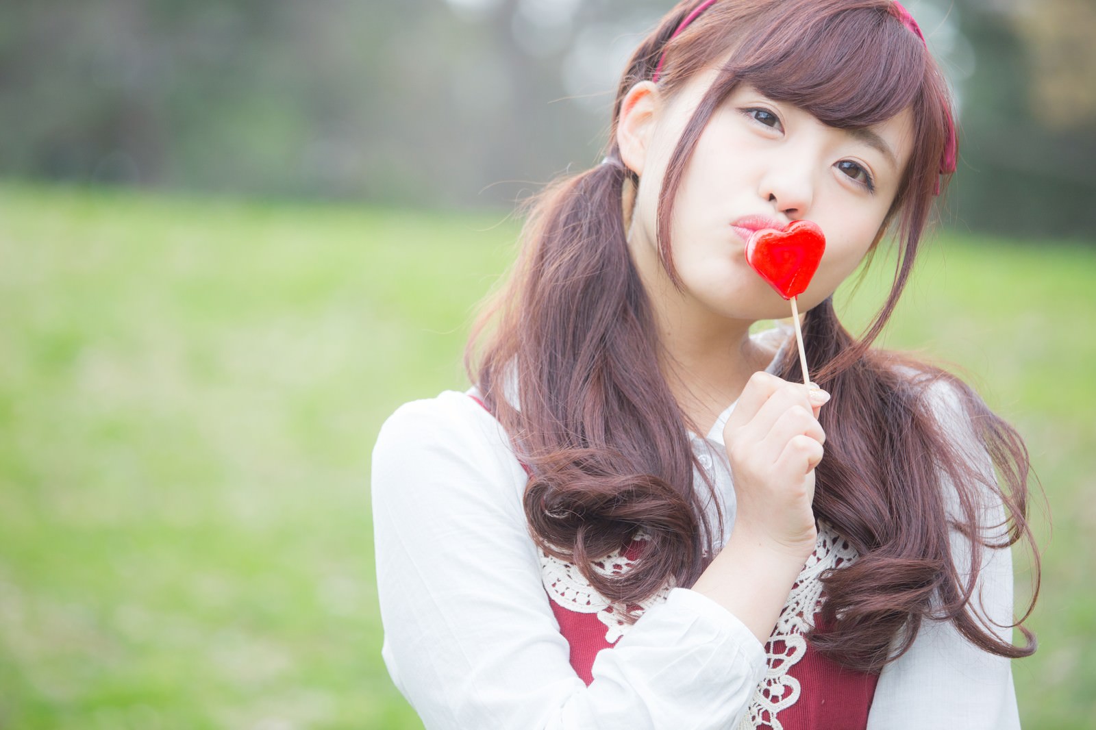 ハート型のキャンディにキスをする、ピンクのヘアピンをした長髪の女の子［モデル：河村友歌］