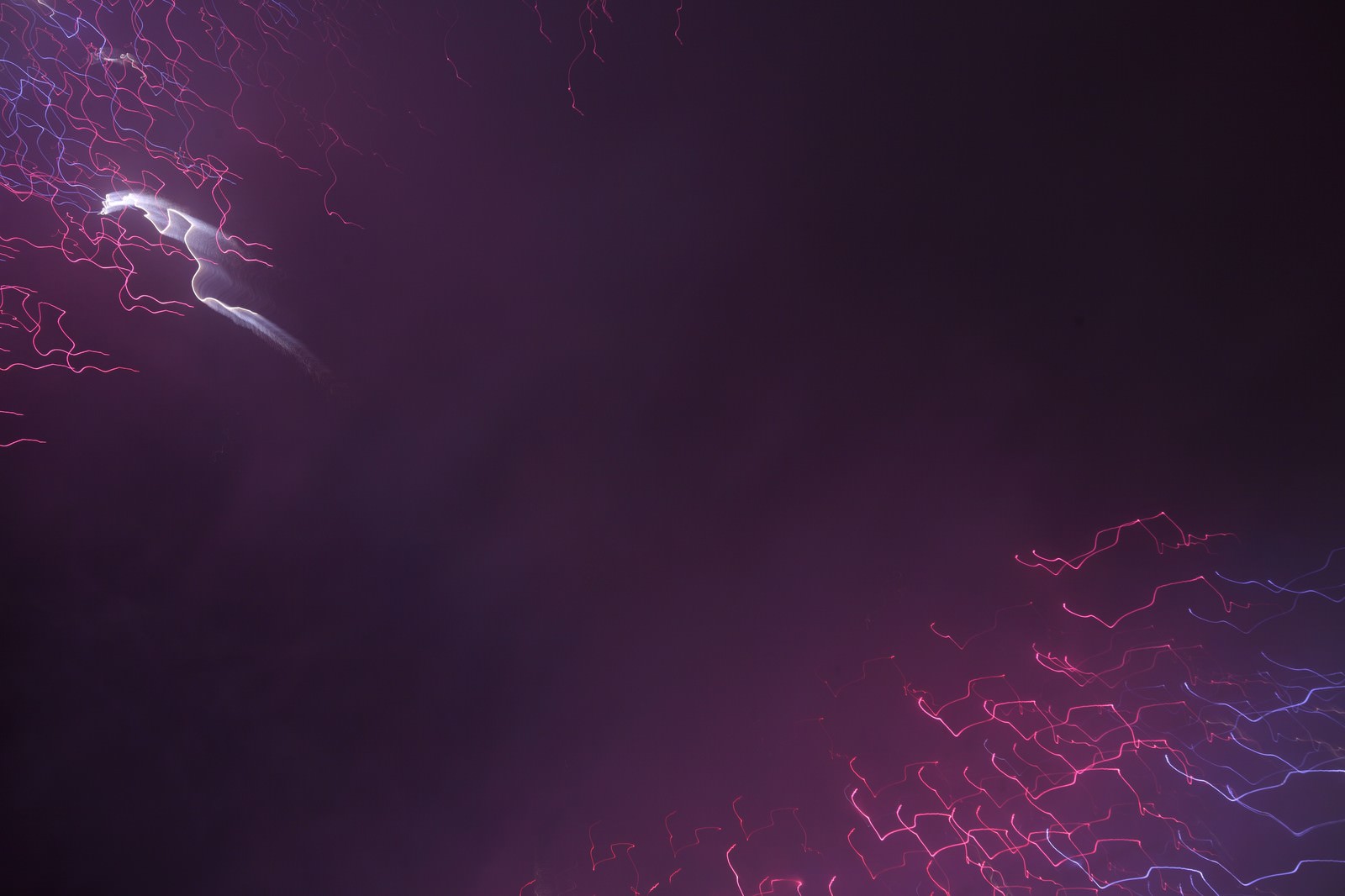 夜空で炸裂する白い花火と赤紫の稲光のような花火