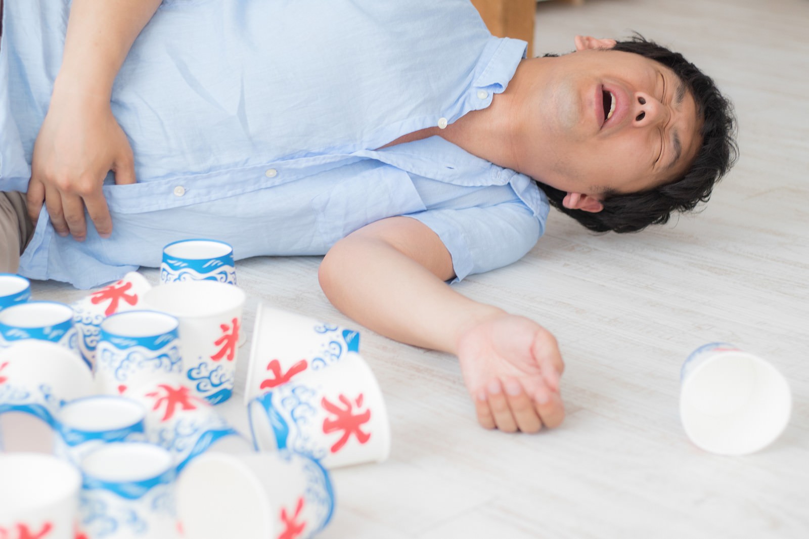 床で腹痛を起こしている男性とかき氷のカップ［モデル：大川竜弥］