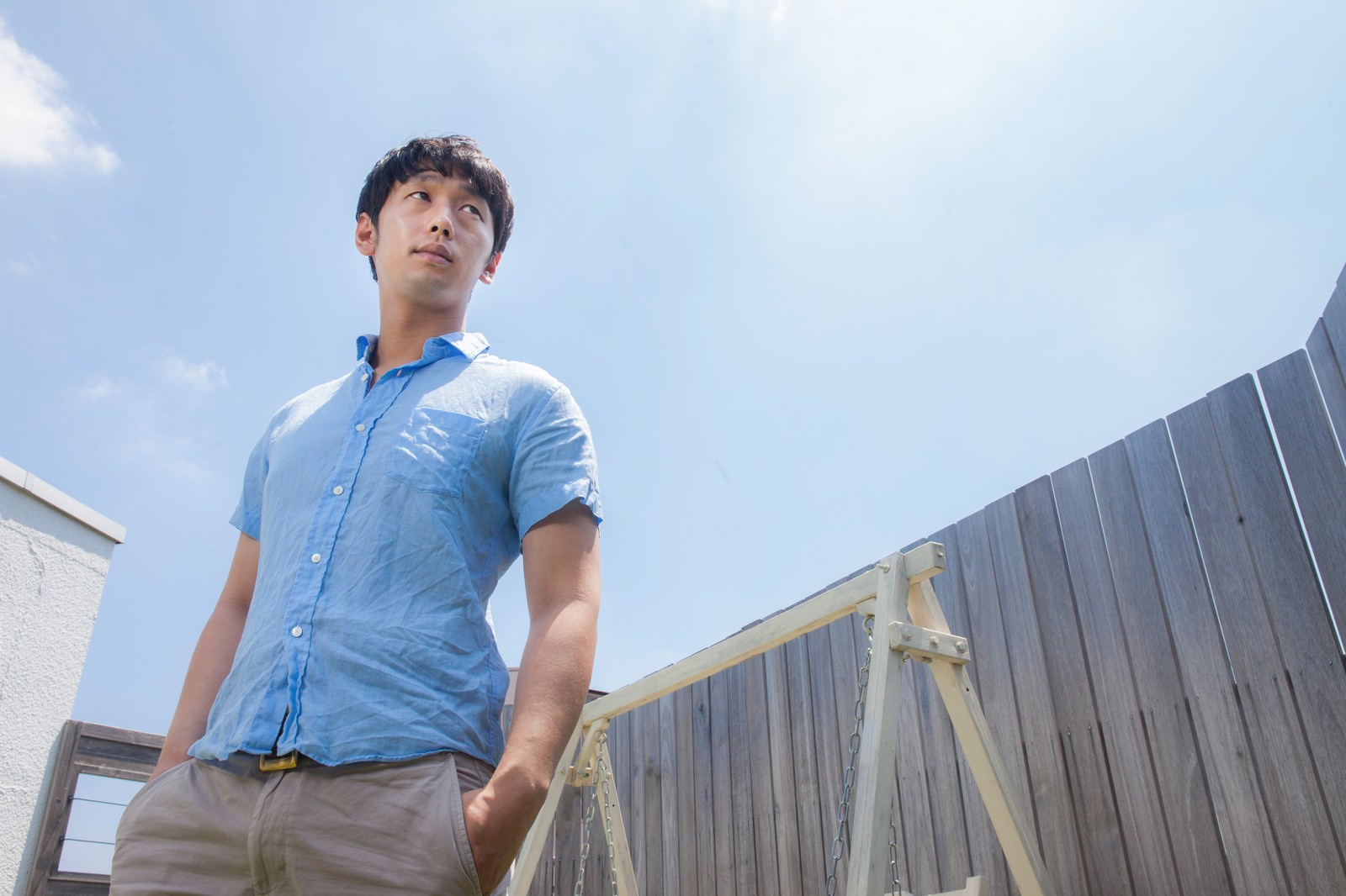 青い半袖シャツを着た男性が晴れた日中、空を見上げている姿勢［モデル：大川竜弥］