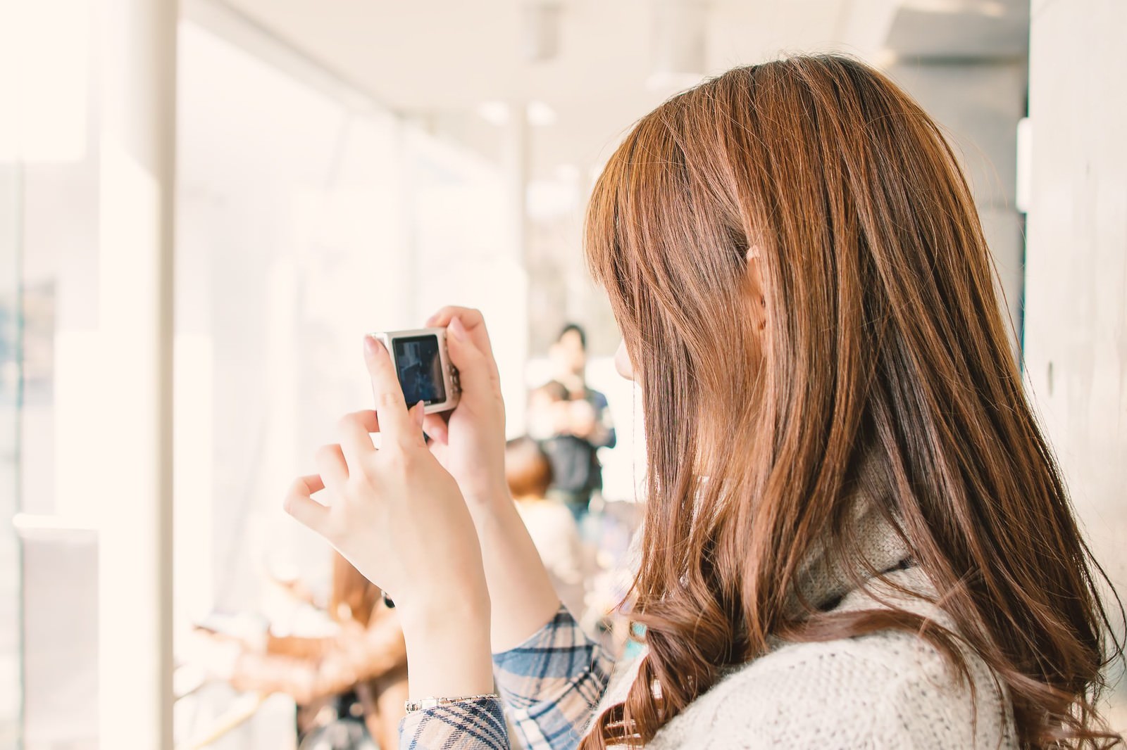 長い茶色の髪の女性がスマートフォンを両手で持ち画面を見ている後ろ姿