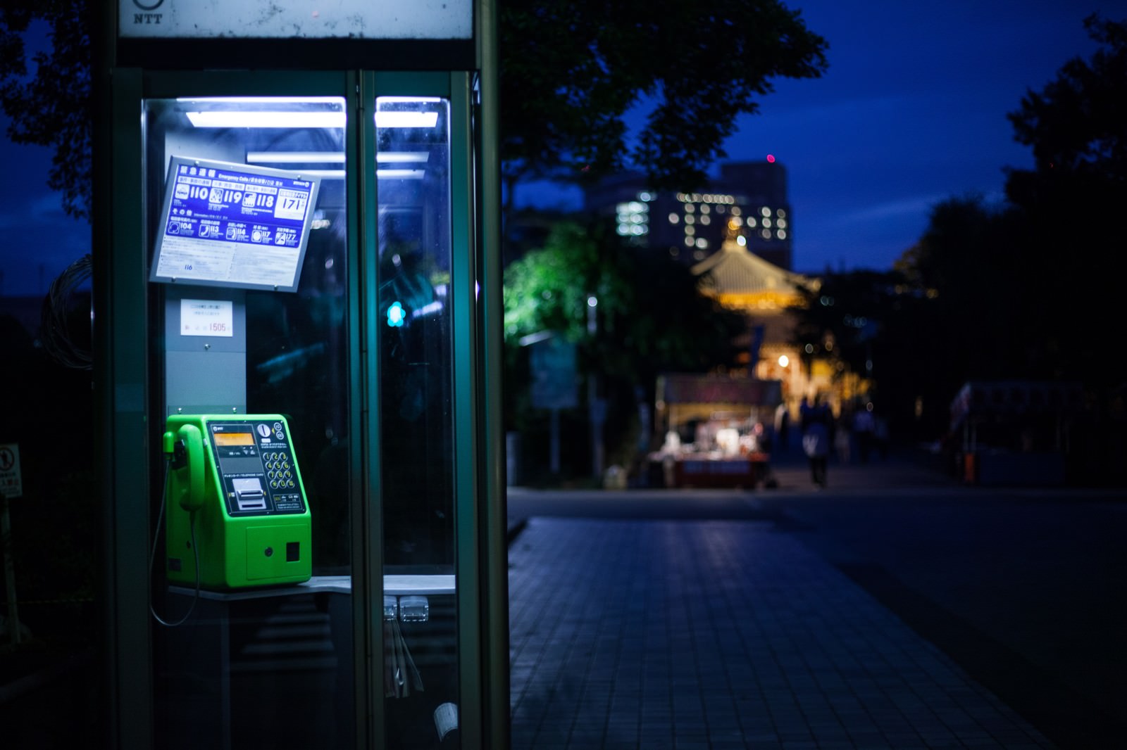 夜間に照らされた緑色の公衆電話ボックス、背景に夜景