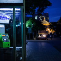 闇夜にてらされる夜間の公衆電話・街灯に照らされた緑色の電話ボックスの写真