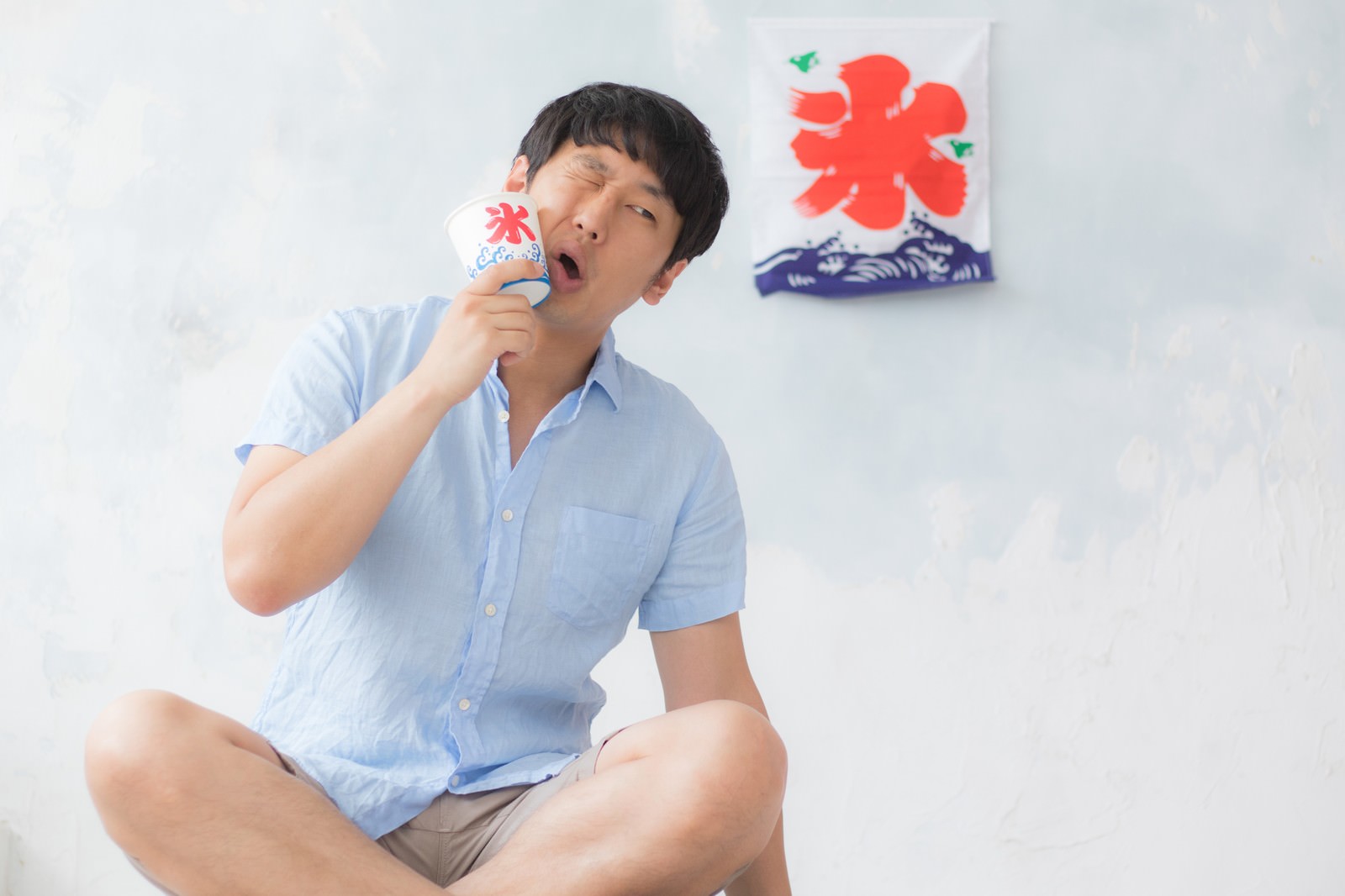 シロップなしのかき氷を食べる薄い青いシャツの男性［モデル：大川竜弥］
