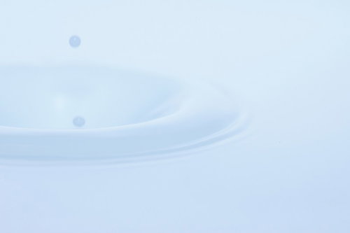青白い色調の水面に落ちた複数の水滴が波紋を広げる接写