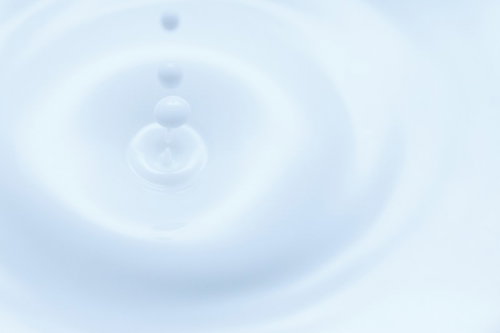 淡い青色の水面に落ちた水滴が波紋を作るミルクドロップの接写