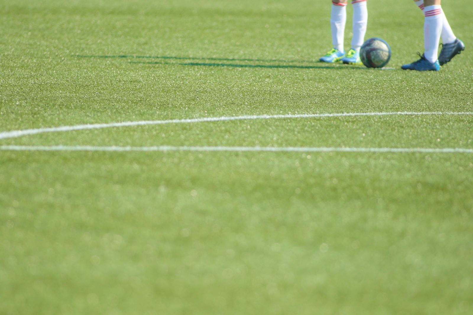 白いラインと選手の足元とボールが写る芝生のサッカーキックオフ