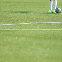 白いラインと選手の足元とボールが写る芝生のサッカーキックオフの写真