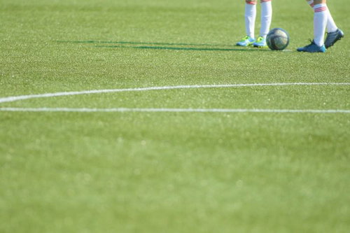 白いラインと選手の足元とボールが写る芝生のサッカーキックオフ