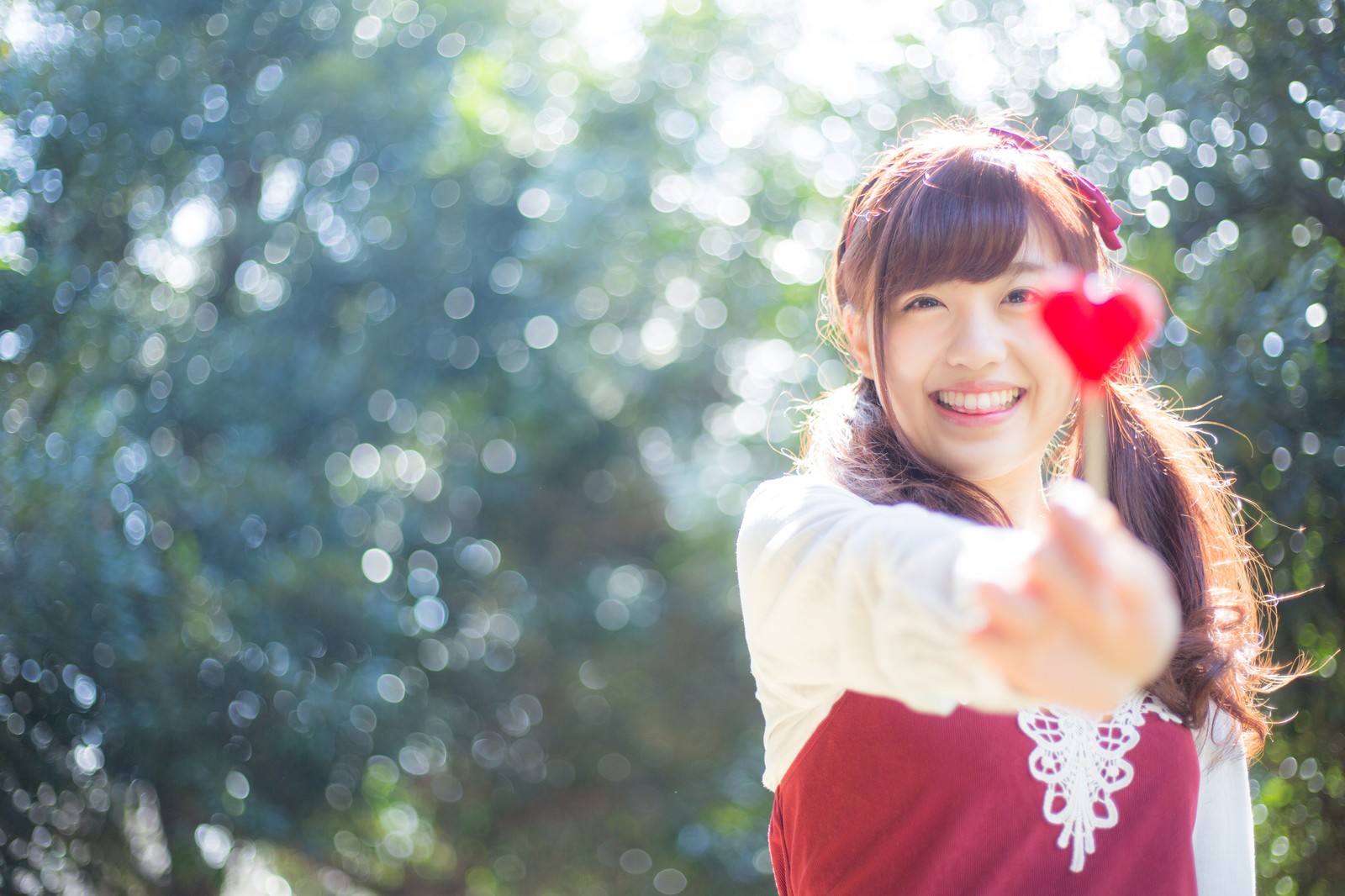 ハート型キャンディを持って笑顔を見せる女性［モデル：河村友歌］