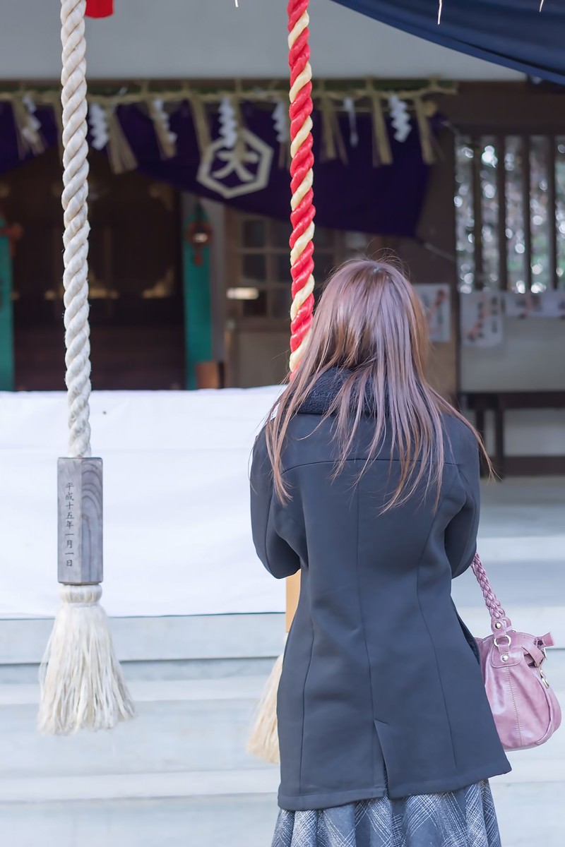 神社の境内で参拝する紺色のジャケット姿の女性