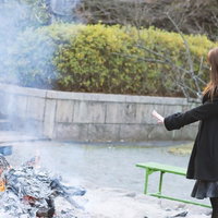 焚き火の前に立つ黒いコートの女性の写真