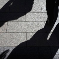 道路に照らされた忍び寄る影、昼間の街中で複数の人影が斜めに伸びるシルエットの写真
