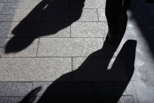 道路に照らされた忍び寄る影、昼間の街中で複数の人影が斜めに伸びるシルエット
