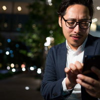 夜間の街で二次会の場所をアプリで必死に探す上司の写真