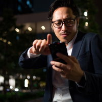 夜間に路上でスワイプをしまくる男性のスマートフォン操作の写真