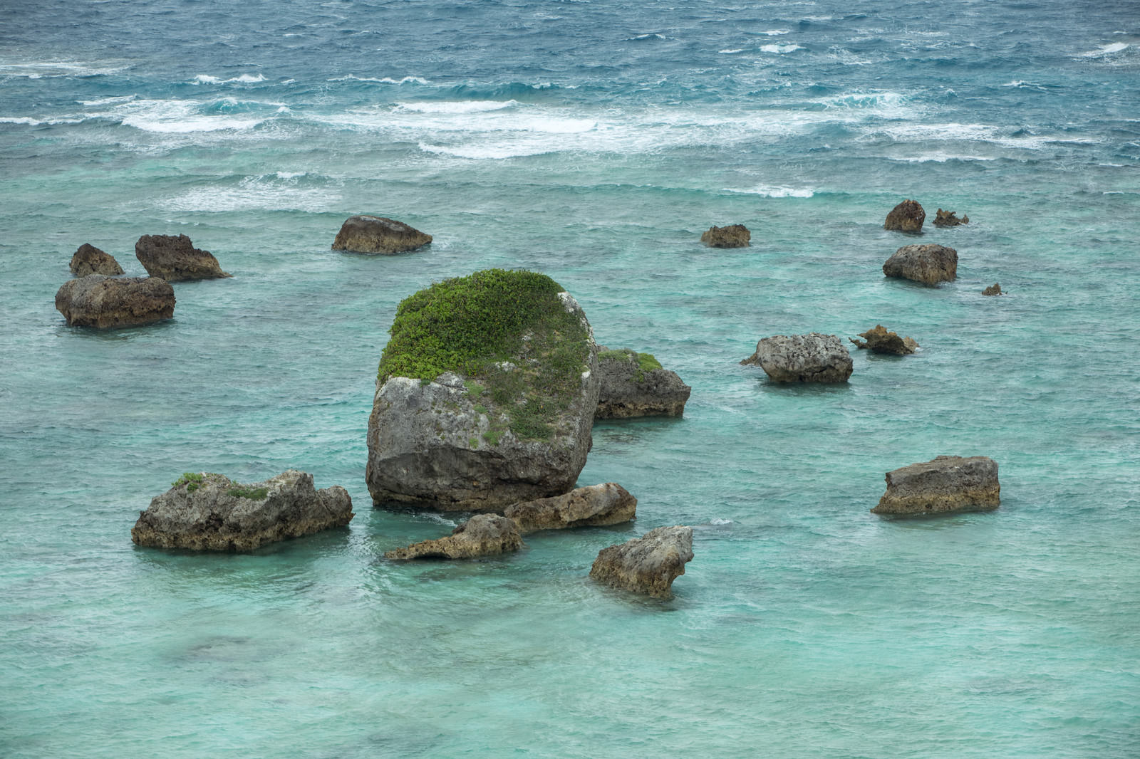 宮古島の浅瀬に点在する苔の生えた岩と青い海