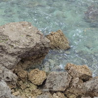 崖下の透明度高い海と岩場、エメラルドグリーンの海水の写真