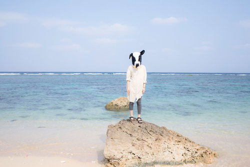 エト牛のぬいぐるみをかぶって宮古島の海と砂浜で両手を広げる人物