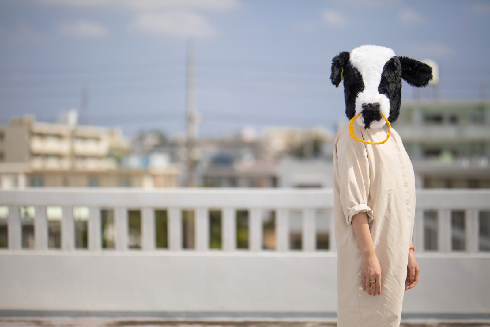 牛のかぶりものをした人がワンピース姿で屋上に立っている