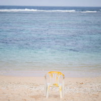 宮古島の波打ち際の砂浜に置かれた白い椅子と青い海の写真
