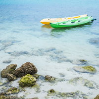 透明な浅瀬に浮かぶ緑と黄色のボートと海底の岩の写真