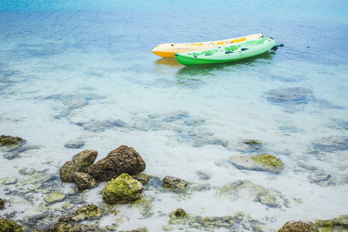 透明な浅瀬に浮かぶ緑と黄色のボートと海底の岩