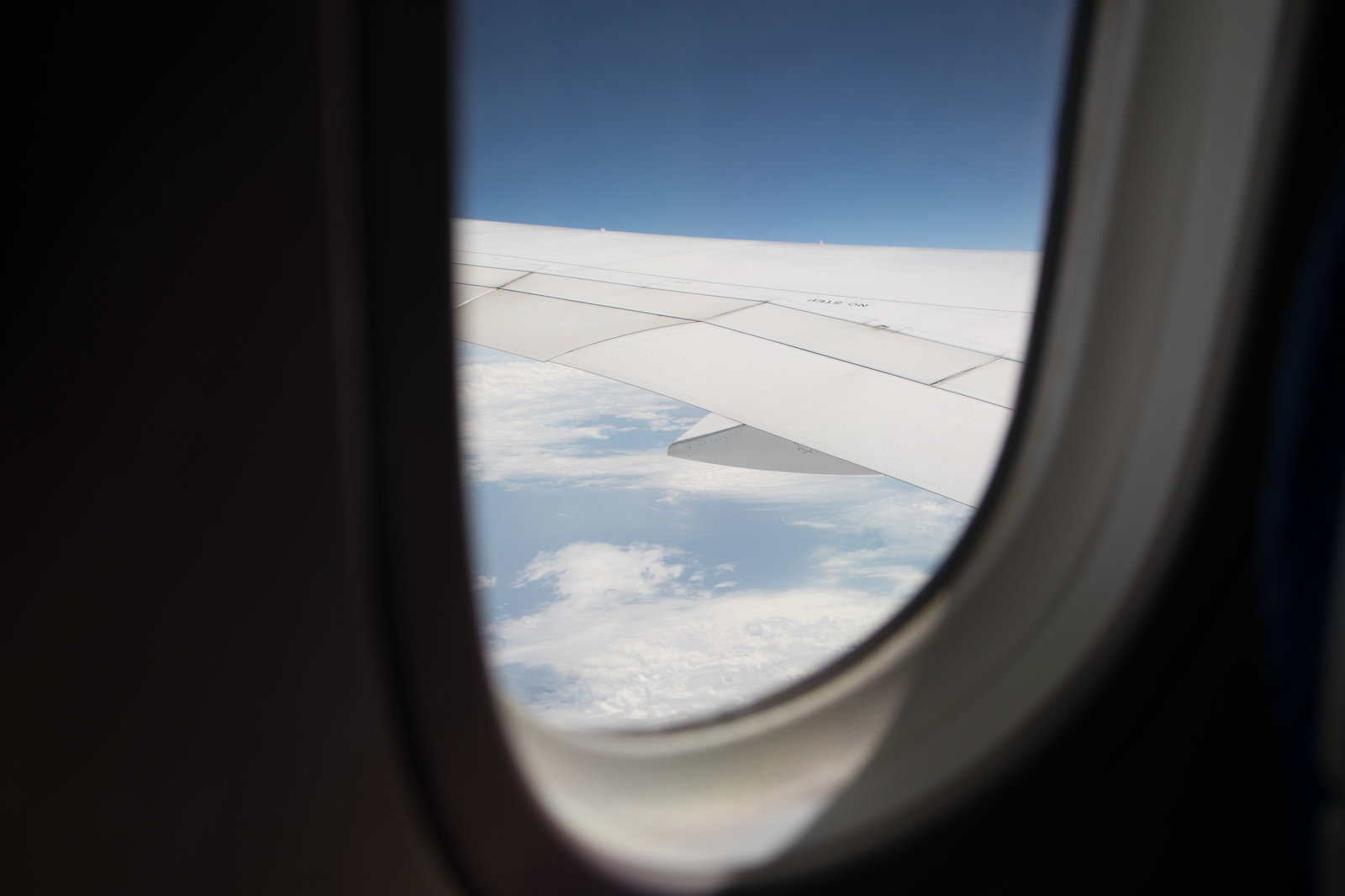 飛行機の窓から見える青空と雲海、翼の一部が写る機内からの眺め