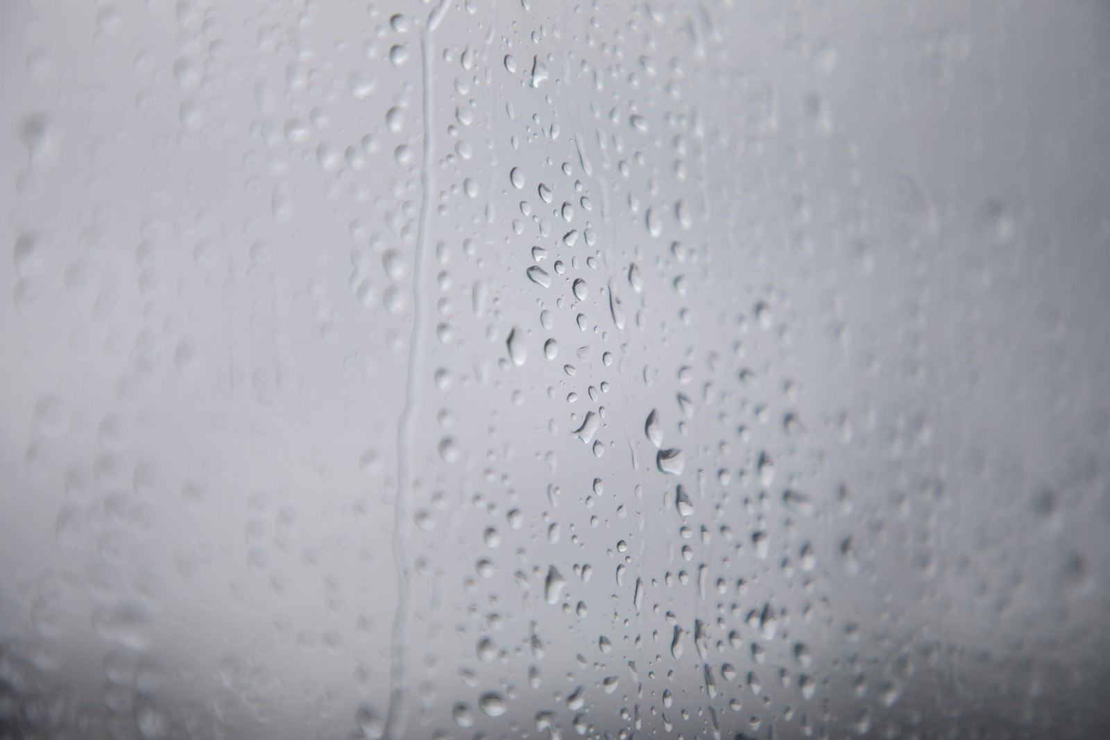 窓ガラスに付着した大小の雨粒と曇り空の背景