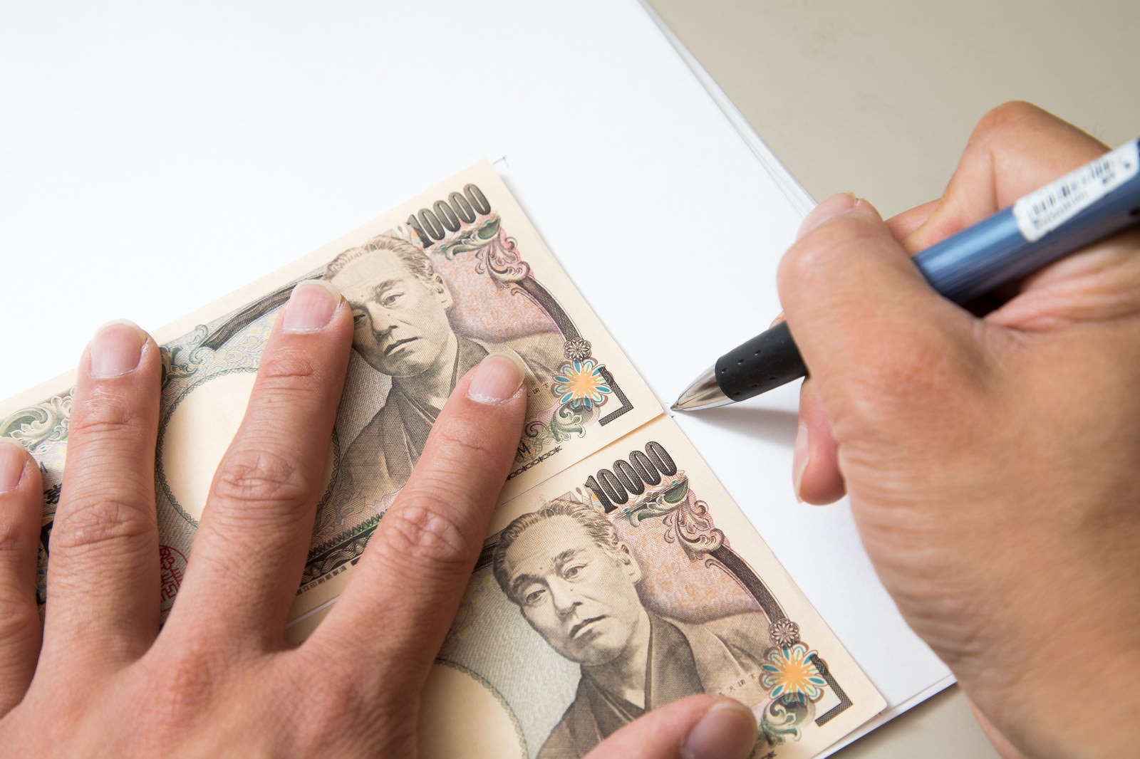 白い紙の上の1万円札をペンでトレースしている手元の様子