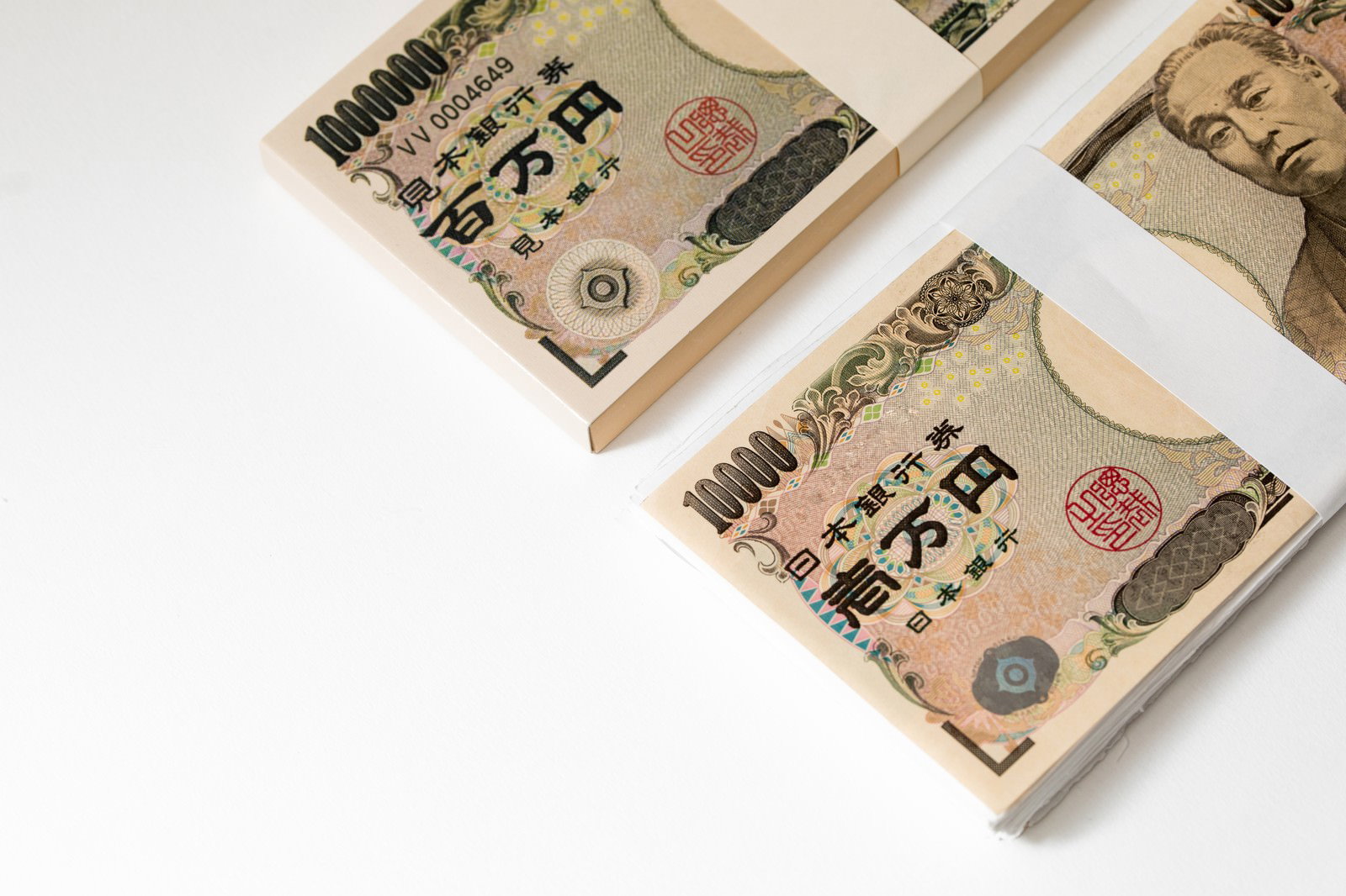 白い背景に偽札の束と本物の1万円札が1枚並べて置かれた状態