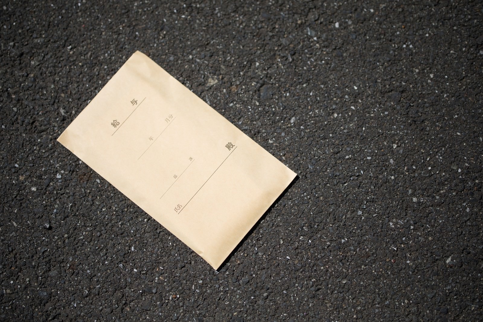 アスファルトの道路に落ちている茶色い給料袋