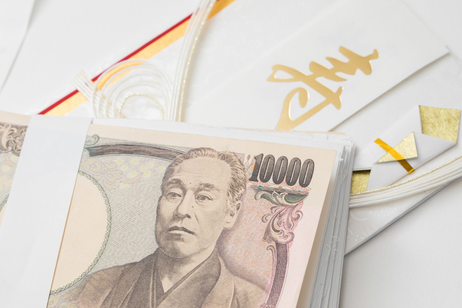 白いご祝儀袋に金色の寿の文字と1万円札束が重ねられ、背景に金色リボンと装飾がある