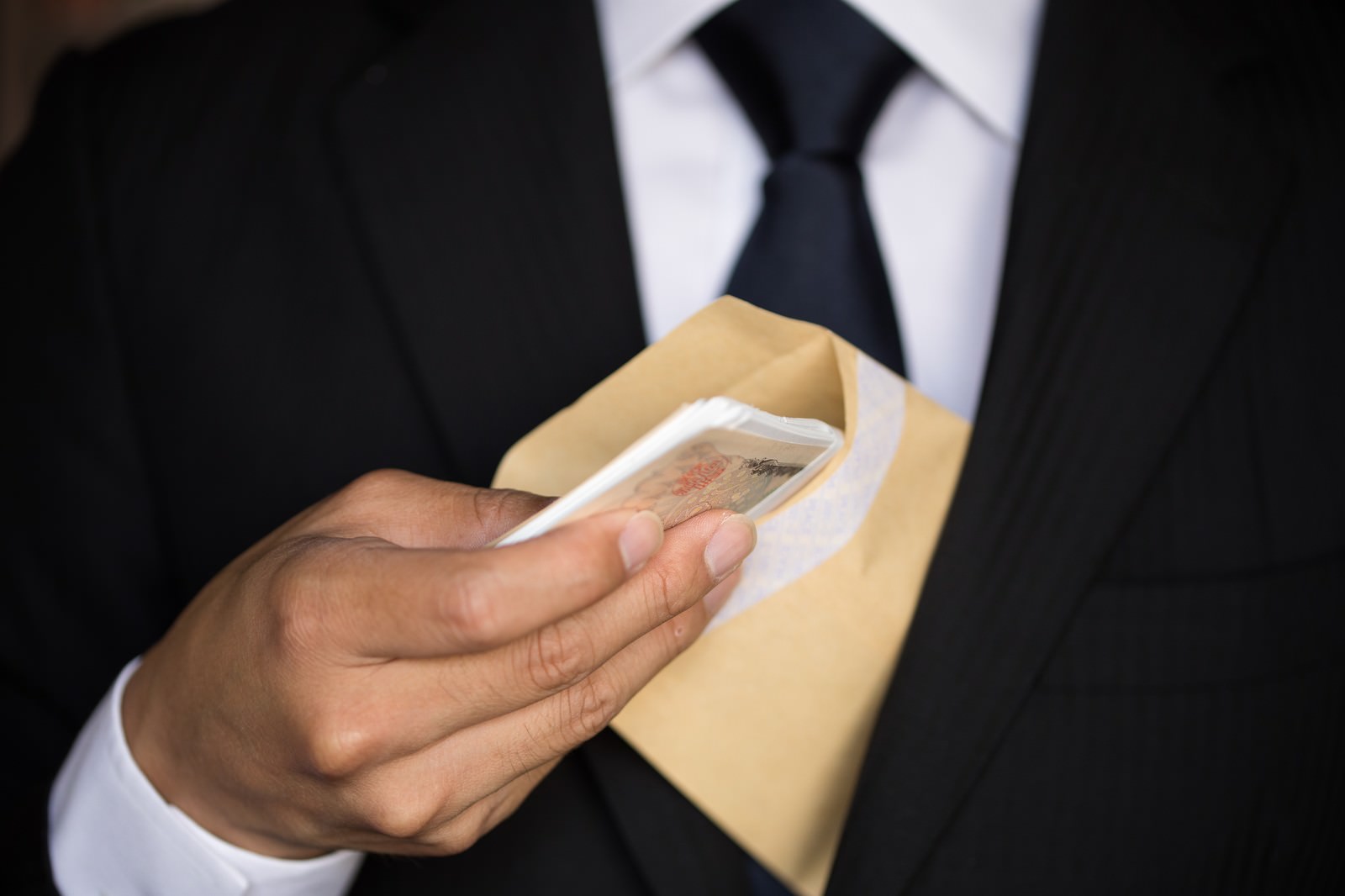 スーツを着た男性が封筒から一万円札の束を取り出している様子