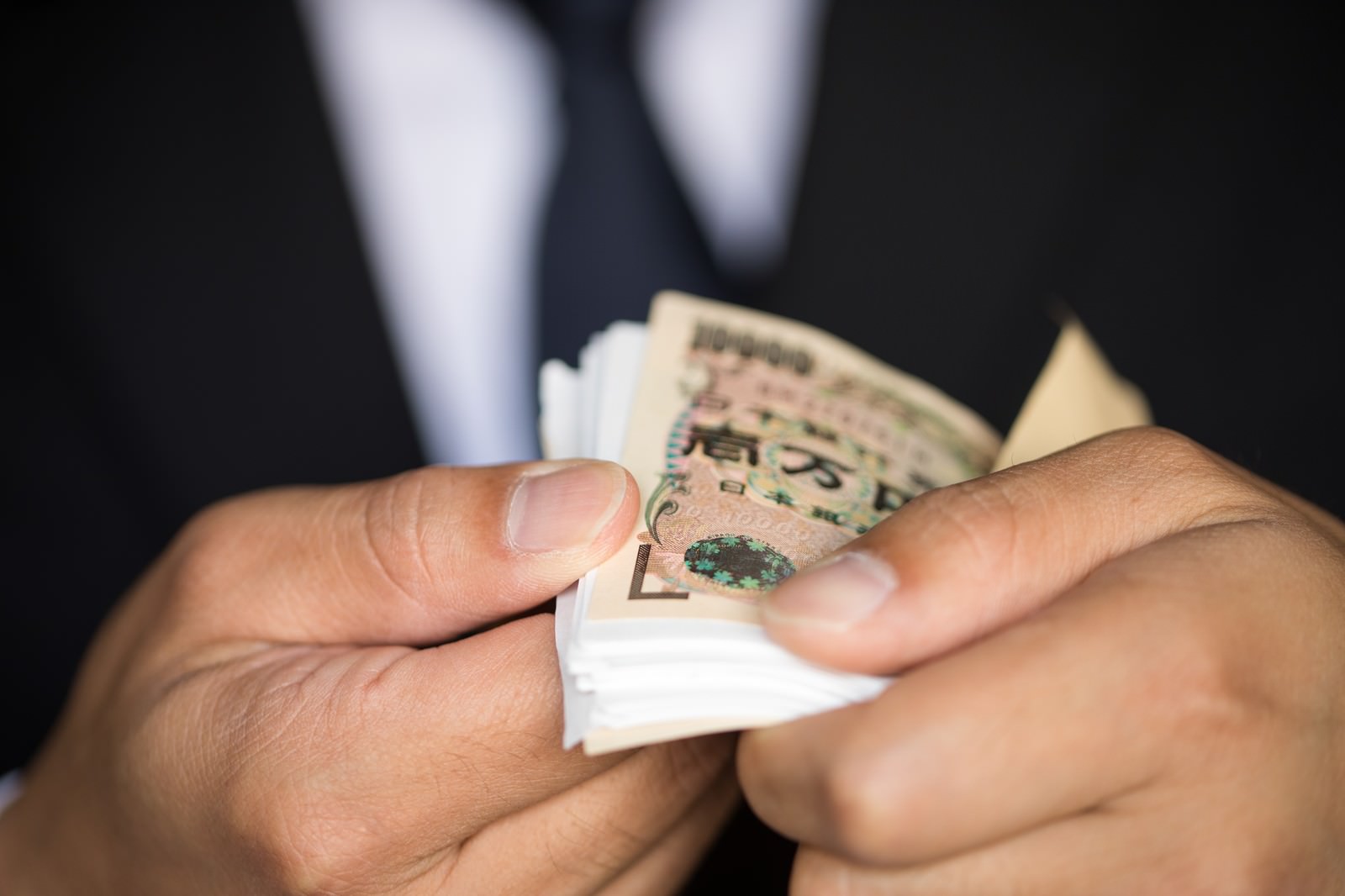 スーツの人物が封筒から取り出した加工済み1万円札の束を両手で握る