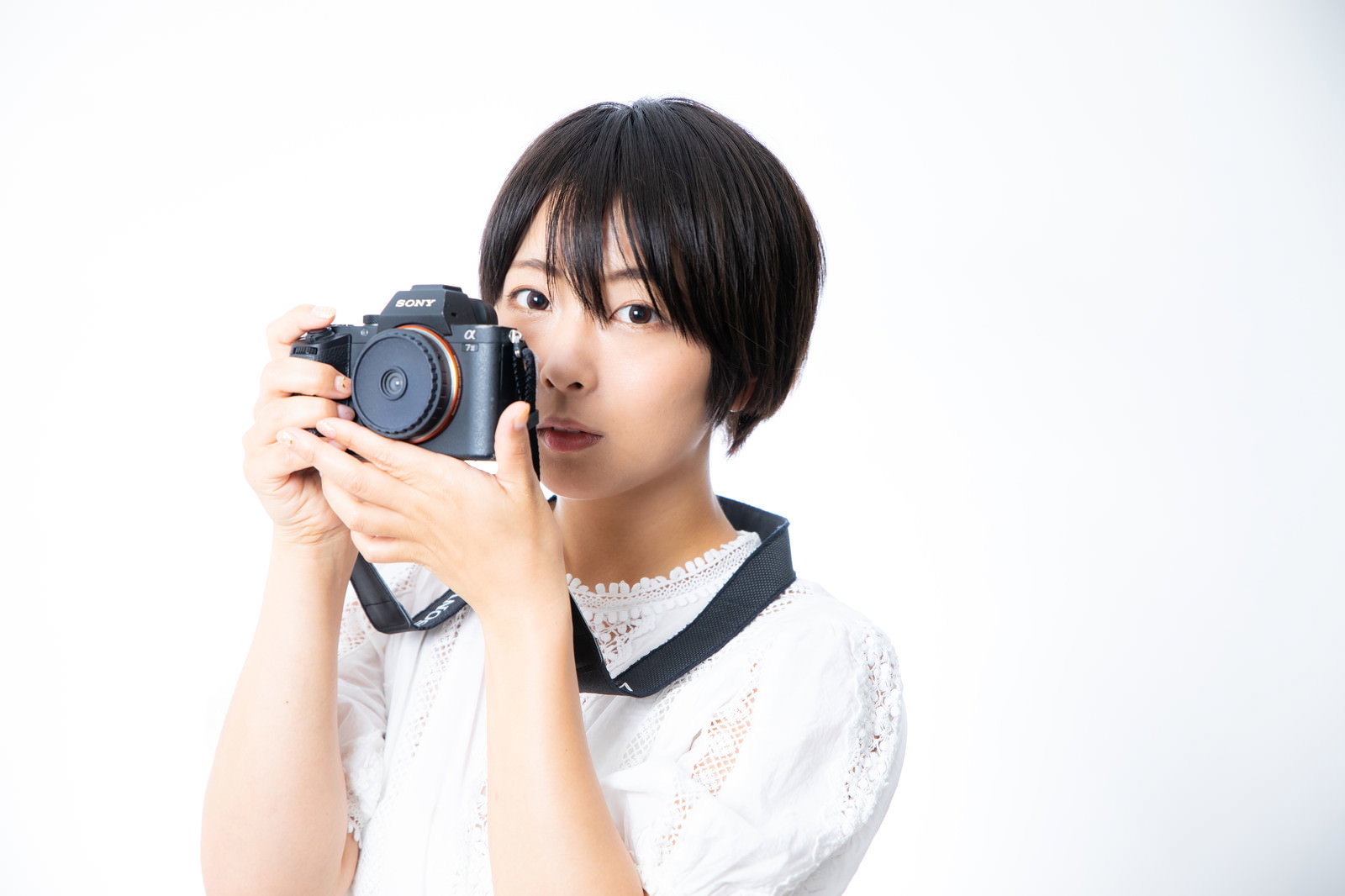 ミラーレスカメラを構えて撮影している白いトップスの女性［モデル：にゃるる］