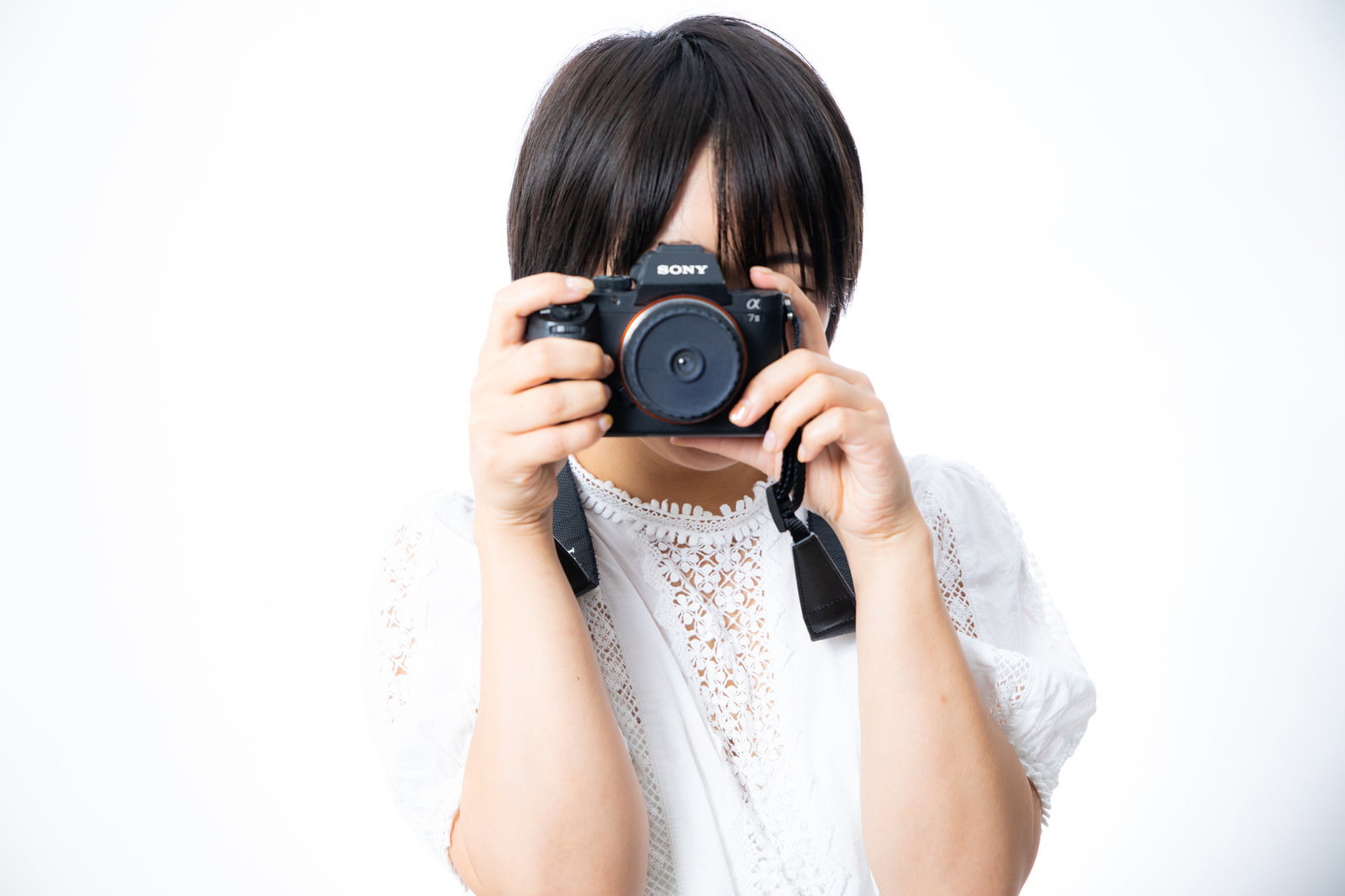 白いトップスを着た女性がカメラのファインダーを覗いている［モデル：にゃるる］