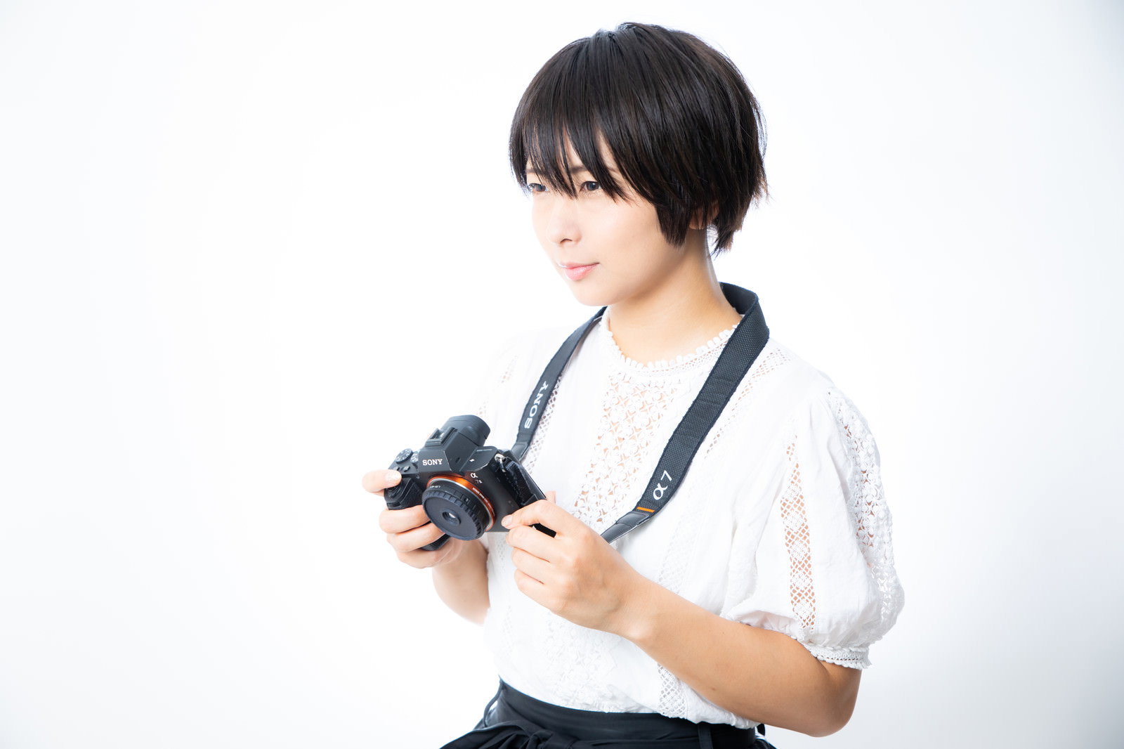 白いシャツを着た女性が黒いミラーレスカメラを構えて撮影している［モデル：にゃるる］