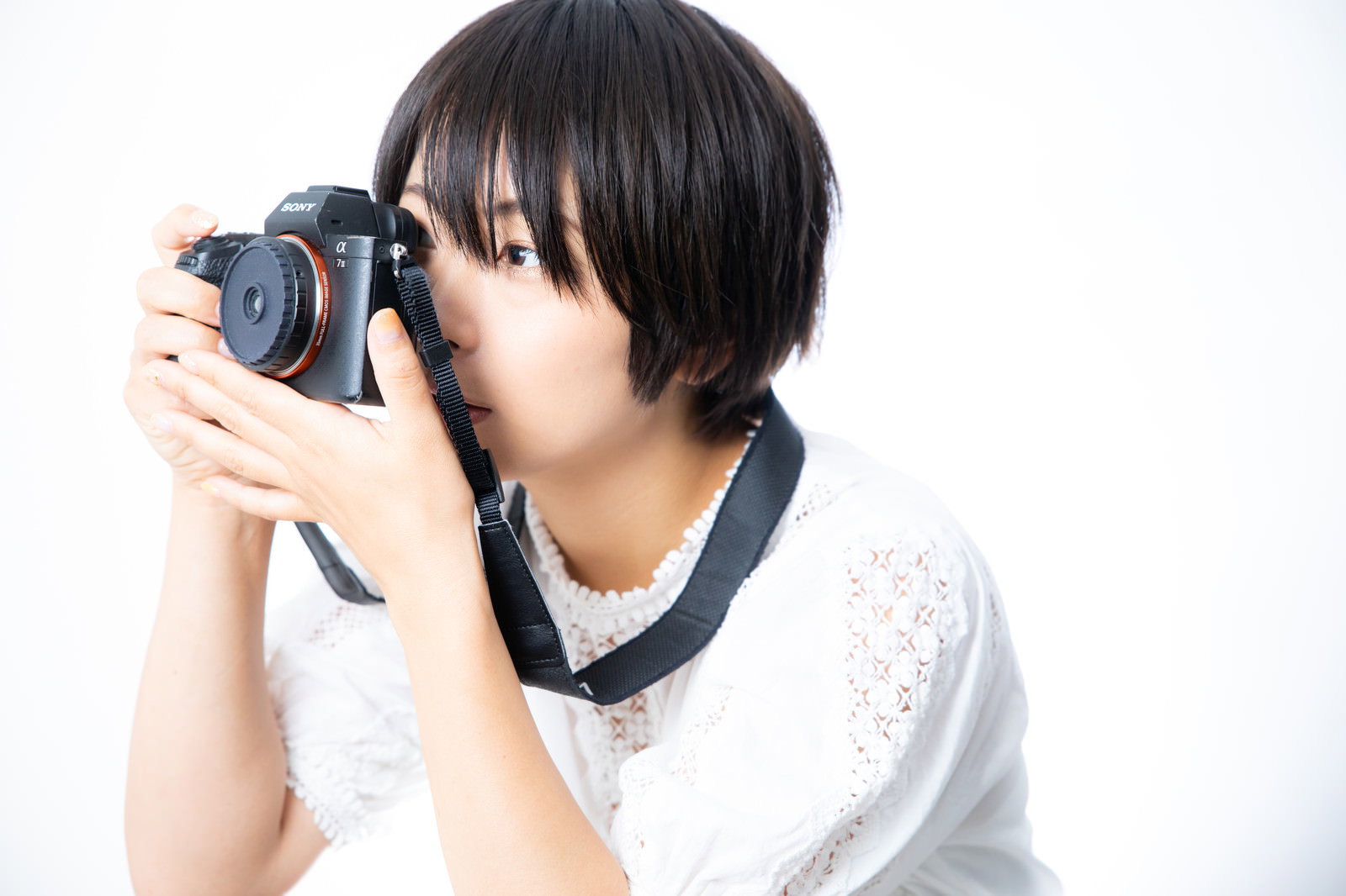 ミラーレスカメラのファインダーを覗いて撮影する女性［モデル：にゃるる］