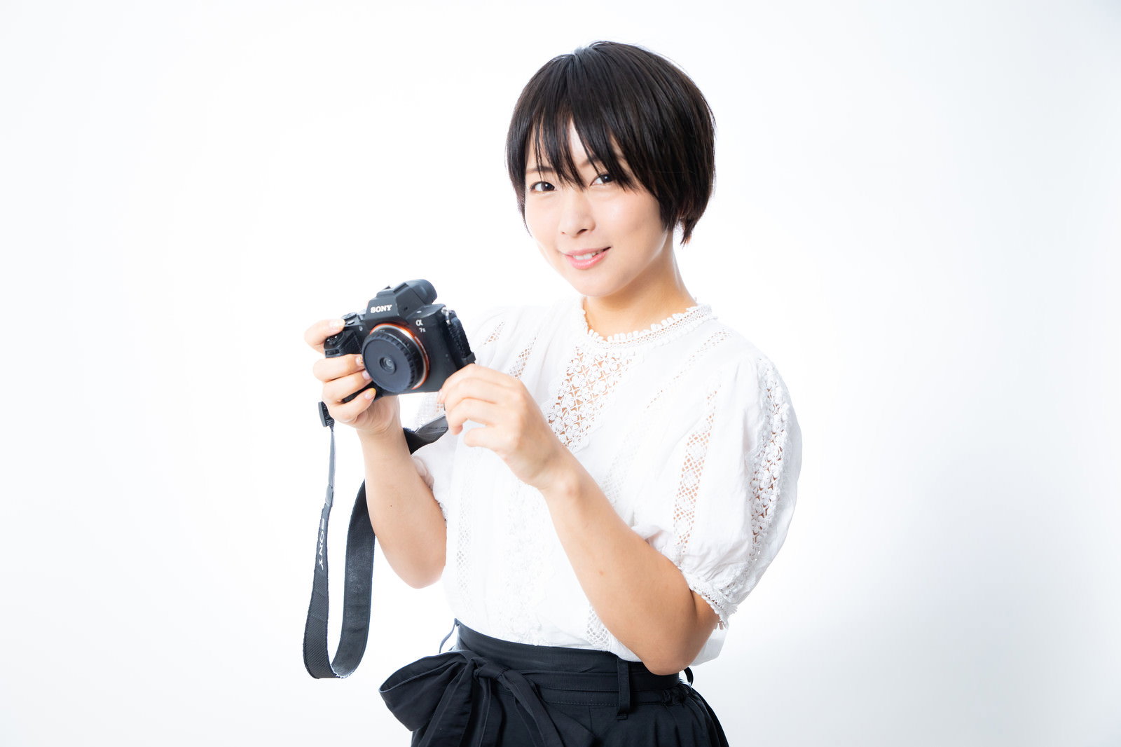 デジタルカメラを手に持ち液晶画面を見て微笑む白いトップスの女性［モデル：にゃるる］