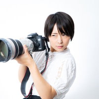 白い望遠レンズを装着した一眼レフカメラを重たそうに持つカメラ女子の写真