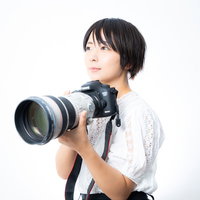 白い望遠レンズを構える満足げなカメラ女子の写真