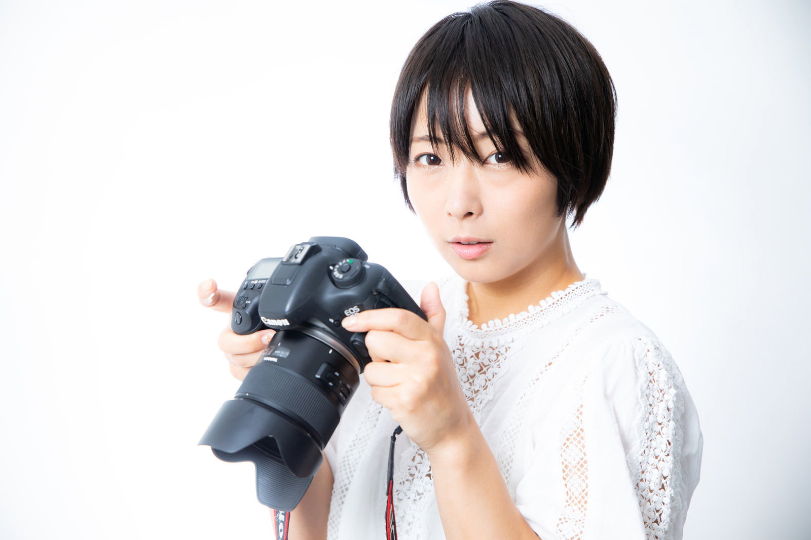 カメラを持って困った表情を見せる白い服の女性［モデル：にゃるる］