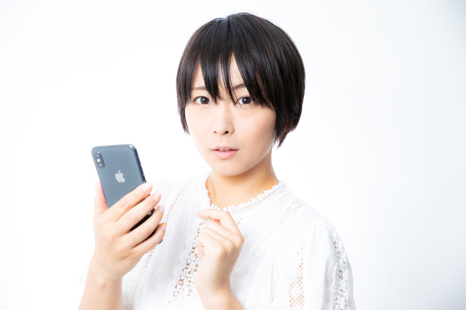 スマートフォンを見てドキッとした表情を浮かべる白い服の女性［モデル：にゃるる］