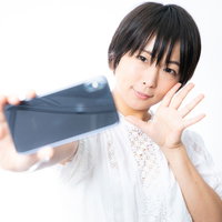 スマホで自撮り中の彼女がピースポーズを取るの写真