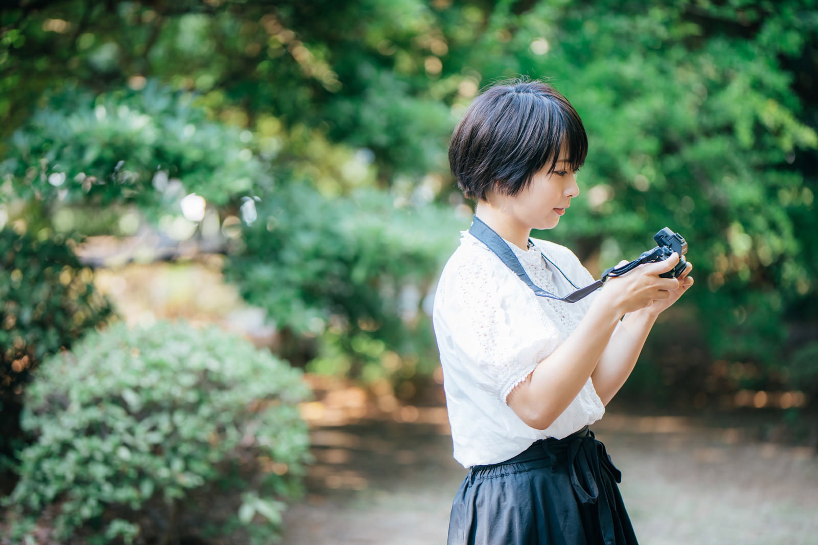 緑の公園でカメラを構えて撮影を楽しむ白いトップスの女性［モデル：にゃるる］