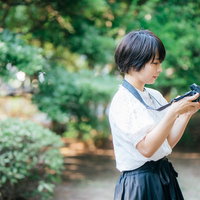 緑の公園でスナップ撮影を楽しむカメラ女子の写真