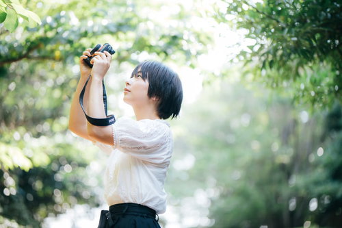 新緑の木漏れ日の中で撮影するカメラ女子のフォトウォーク